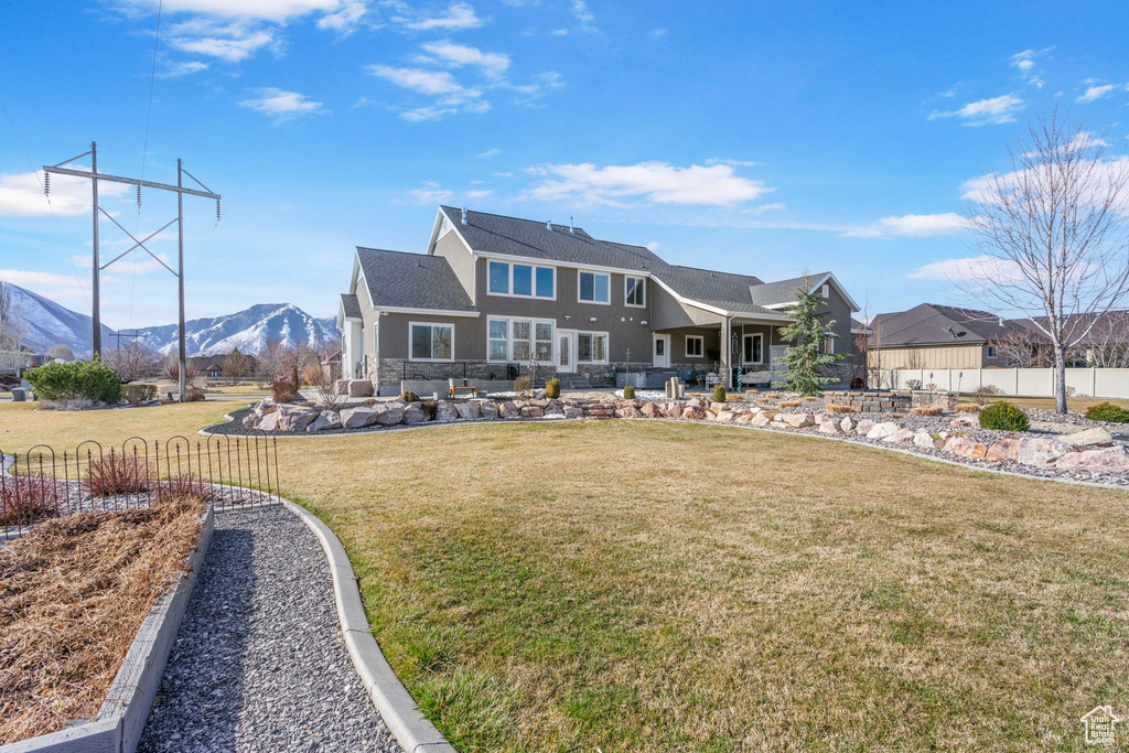 Back of property with stone siding, a lawn, a mountain view, and fence