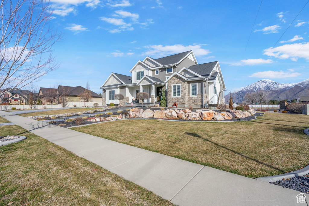 View of front of home featuring stone siding, a mountain view, a front yard, and fence