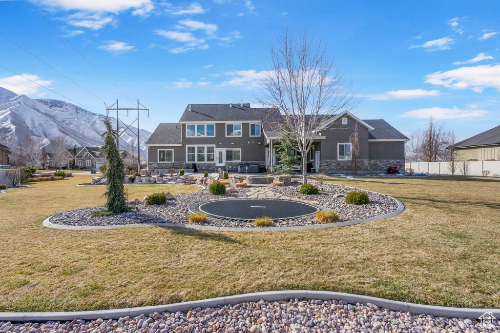 Back of house featuring a mountain view, fence, a lawn, and stone siding