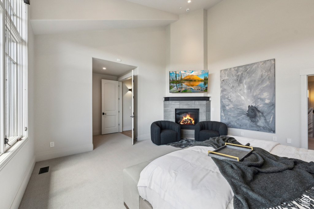 Bedroom with visible vents, baseboards, high vaulted ceiling, light colored carpet, and a tiled fireplace