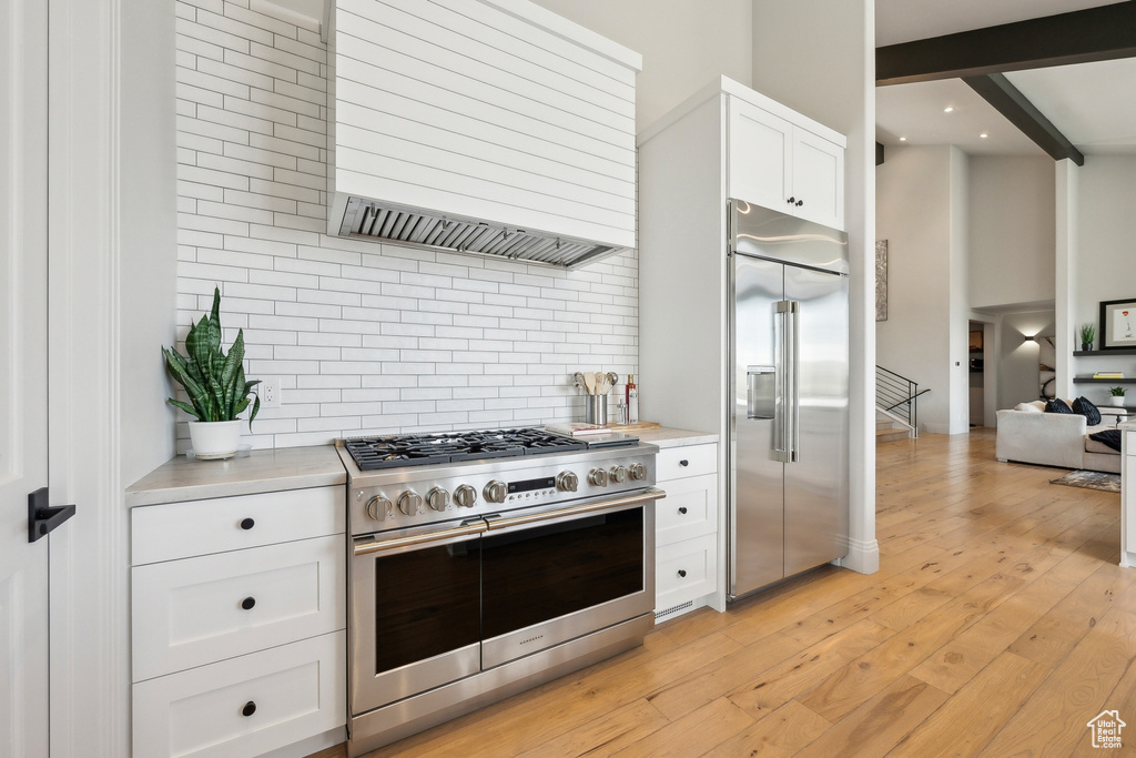 Kitchen featuring light countertops, high quality appliances, wall chimney exhaust hood, and tasteful backsplash