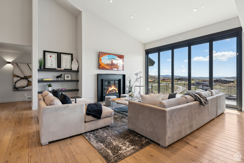 Living area featuring a glass covered fireplace, high vaulted ceiling, recessed lighting, and light wood-type flooring