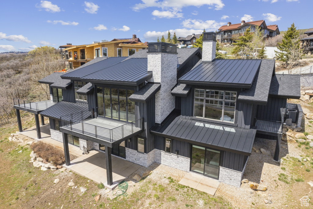 Rear view of property featuring a standing seam roof, board and batten siding, a chimney, and a patio area