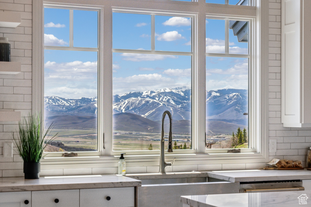 Interior details featuring light stone countertops, white cabinetry, a mountain view, tasteful backsplash, and a sink