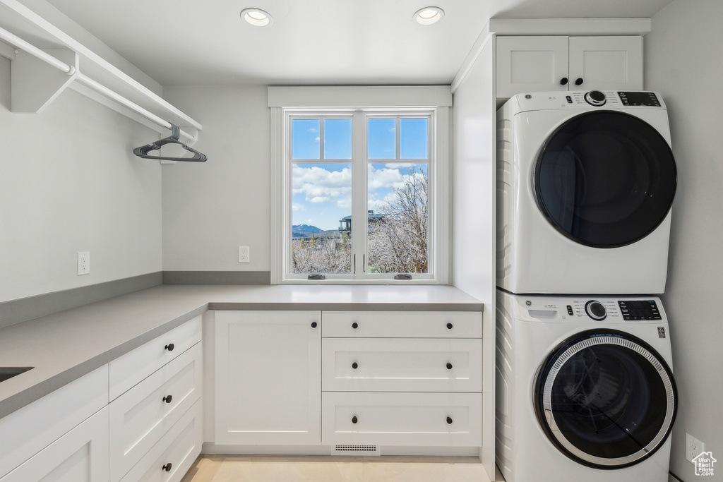 Clothes washing area with cabinet space, recessed lighting, stacked washing maching and dryer, and visible vents
