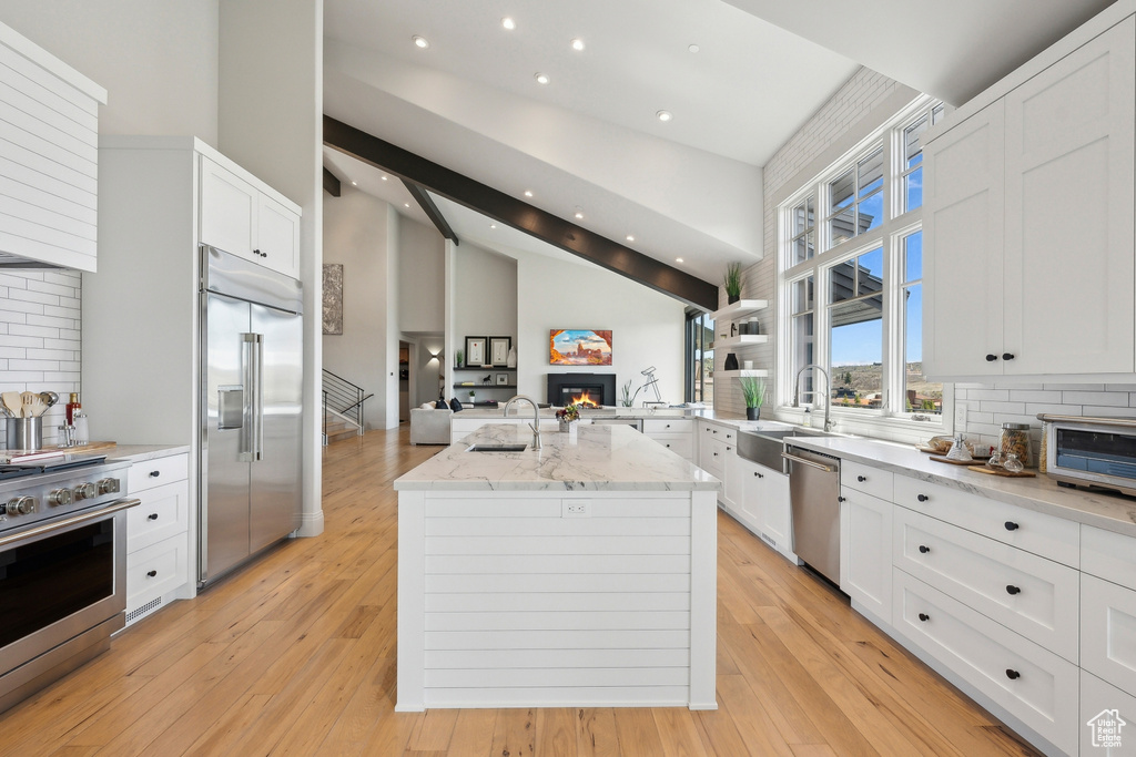 Kitchen featuring a glass covered fireplace, a sink, open floor plan, high quality appliances, and tasteful backsplash