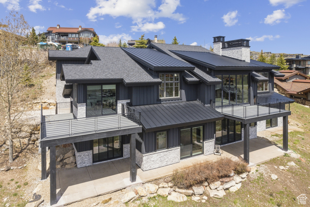 Back of house featuring stone siding, board and batten siding, a chimney, a balcony, and a patio