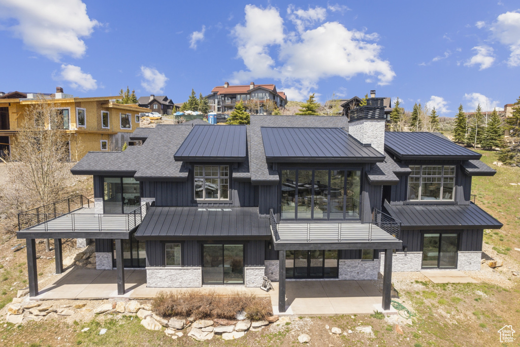 Back of property featuring board and batten siding, a standing seam roof, a chimney, a patio area, and a balcony