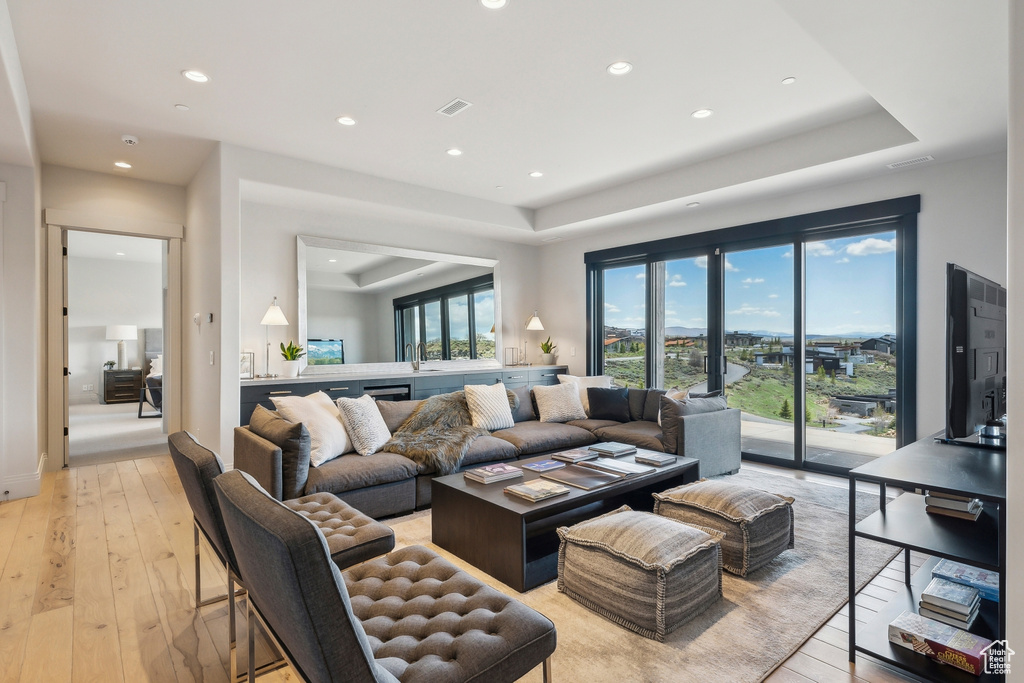 Living room with light wood-style floors, a raised ceiling, and recessed lighting