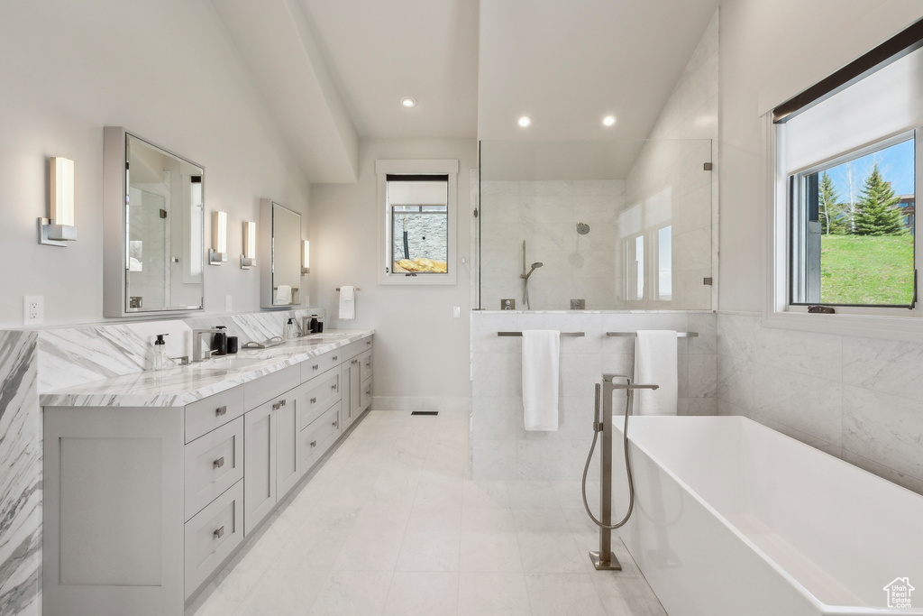 Full bath featuring double vanity, a freestanding tub, tile walls, a walk in shower, and recessed lighting
