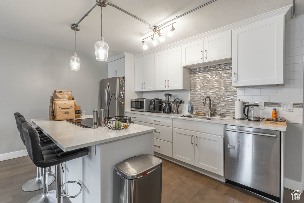 Kitchen with a sink, decorative backsplash, dark wood-type flooring, white cabinets, and appliances with stainless steel finishes