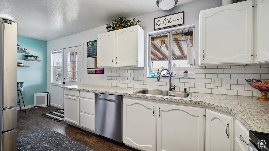 Kitchen with backsplash, appliances with stainless steel finishes, dark wood-style floors, white cabinetry, and a sink