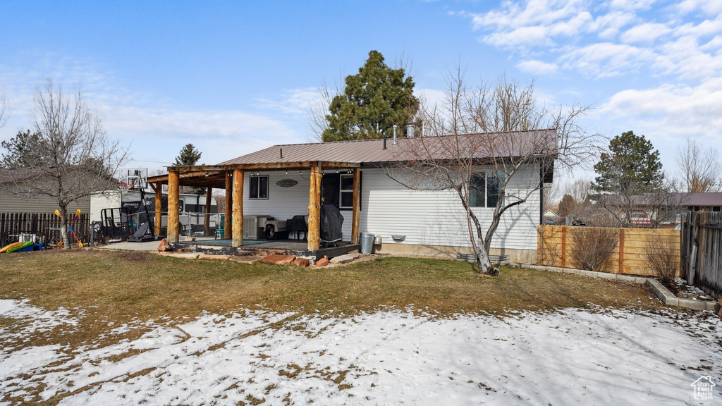 Snow covered rear of property with a yard, a fenced backyard, a playground, a patio area, and metal roof
