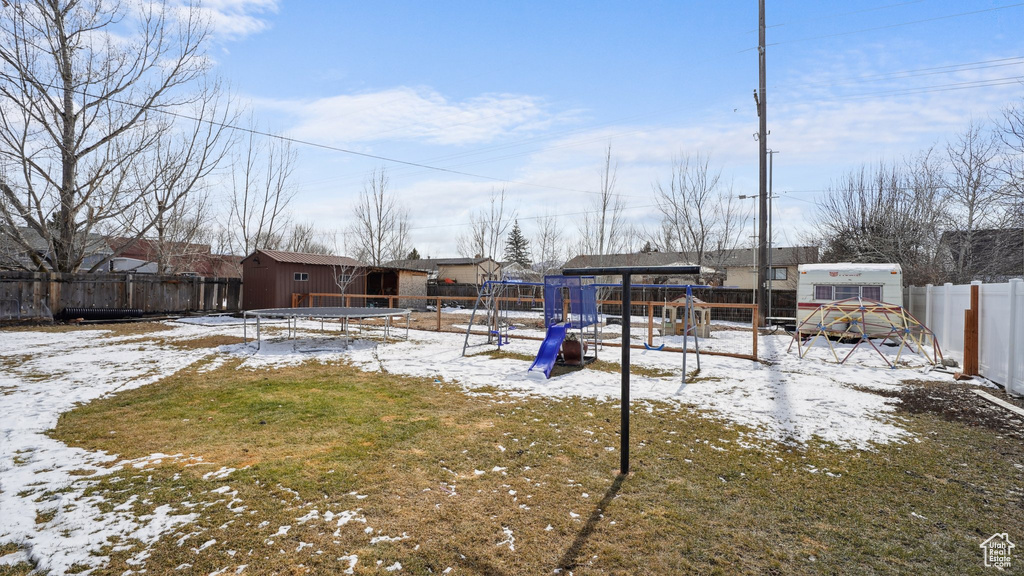 Yard layered in snow with an outbuilding, a fenced backyard, a shed, and a playground