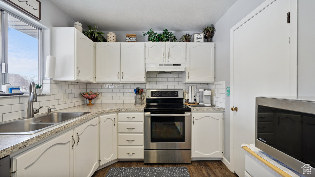 Kitchen with a sink, under cabinet range hood, stainless steel appliances, white cabinets, and light countertops