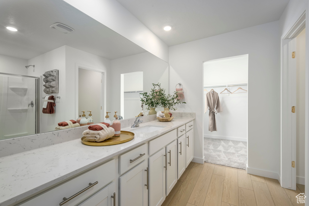 Bathroom featuring a walk in closet, a stall shower, wood finished floors, recessed lighting, and vanity