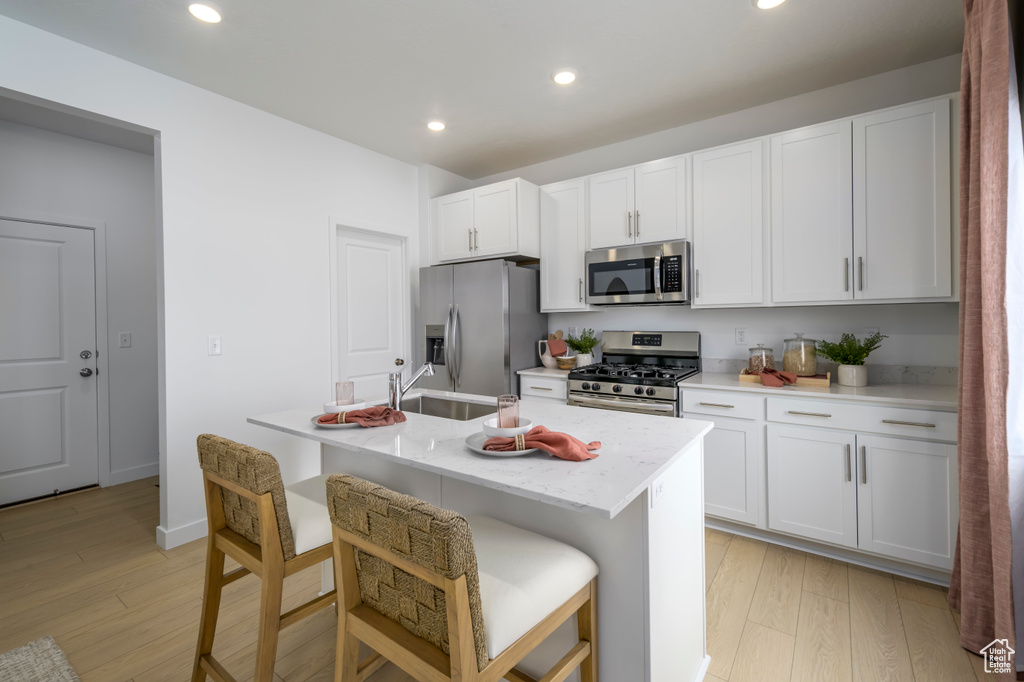 Kitchen with light wood-type flooring, an island with sink, recessed lighting, appliances with stainless steel finishes, and white cabinets