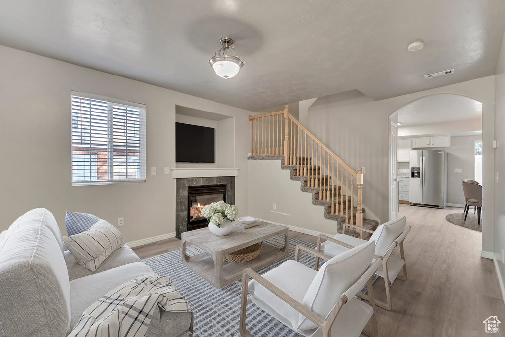 Living room with light wood-type flooring, visible vents, arched walkways, baseboards, and a tile fireplace