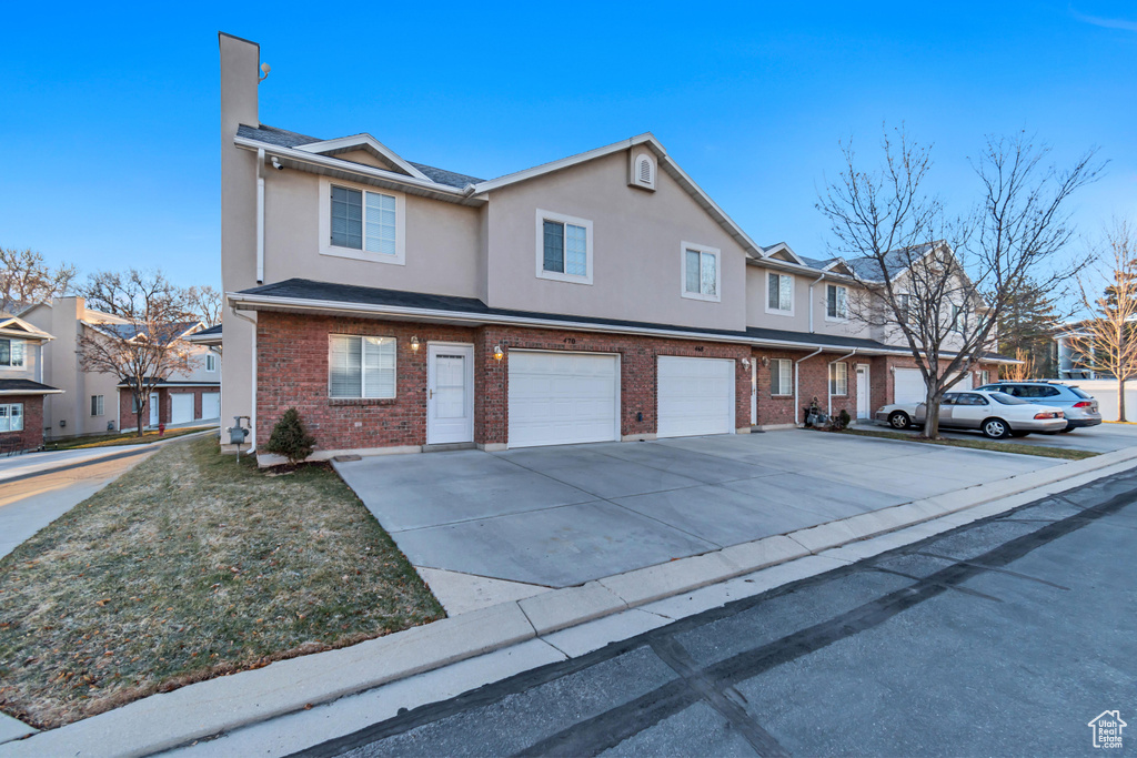 Townhome / multi-family property with a garage, brick siding, driveway, and stucco siding