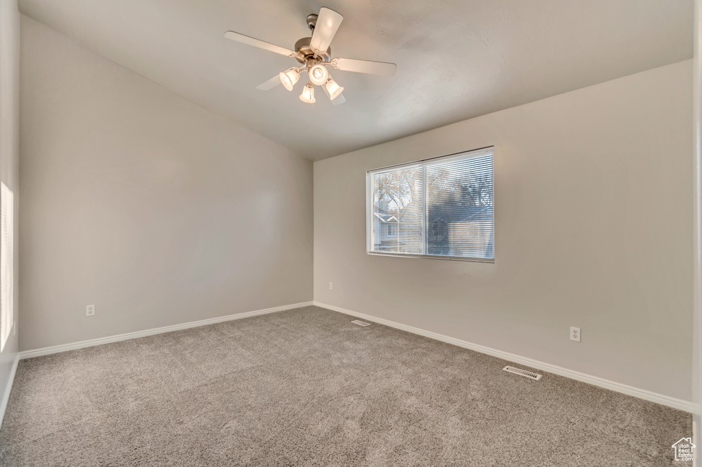 Carpeted spare room with visible vents, baseboards, lofted ceiling, and a ceiling fan