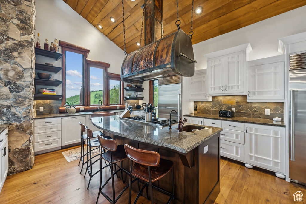 Kitchen featuring wood ceiling, open shelves, appliances with stainless steel finishes, white cabinetry, and an island with sink