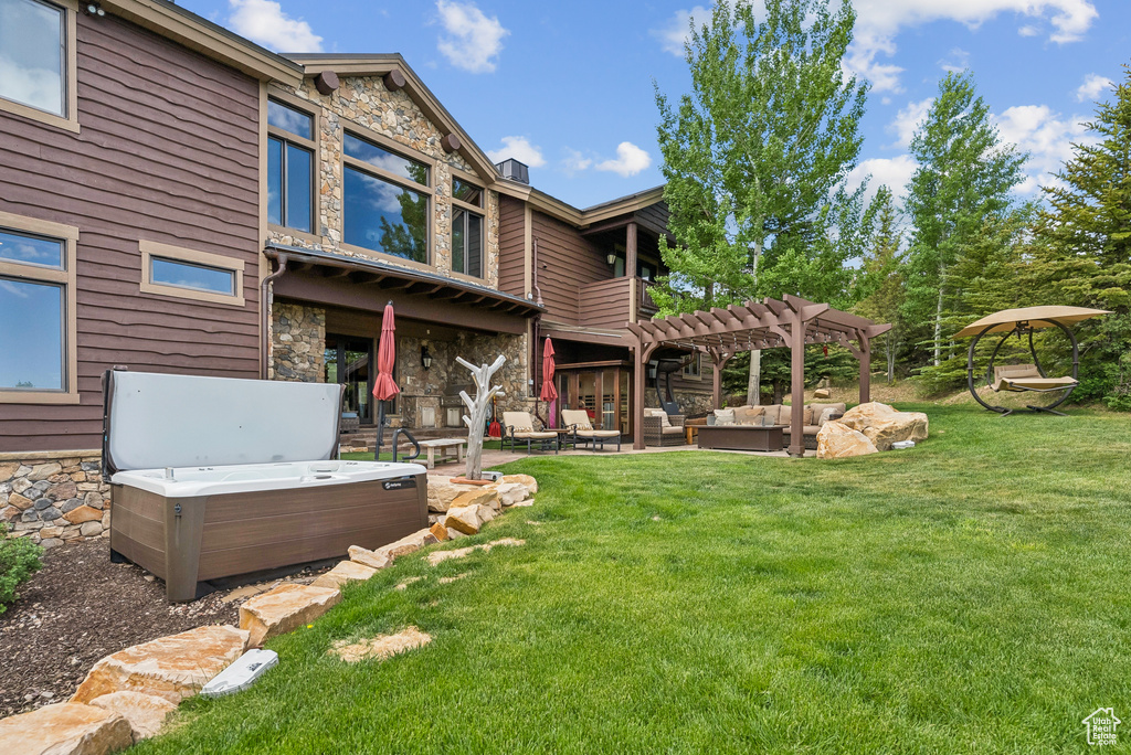 Rear view of house featuring a hot tub, stone siding, outdoor lounge area, and a pergola