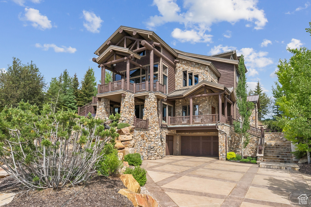 View of front of home with stone siding, an attached garage, a balcony, a standing seam roof, and a metal roof