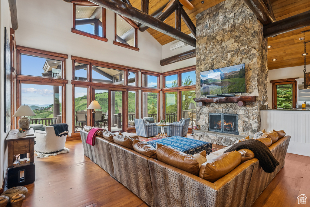 Living area with a stone fireplace, a wood ceiling with exposed beams, high vaulted ceiling, hardwood / wood-style flooring, and healthy amount of natural light