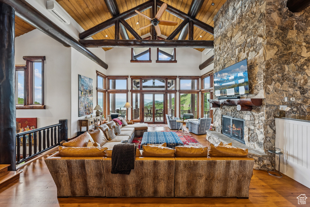 Living area with a wood ceiling with exposed beams, high vaulted ceiling, wood-type flooring, and a stone fireplace