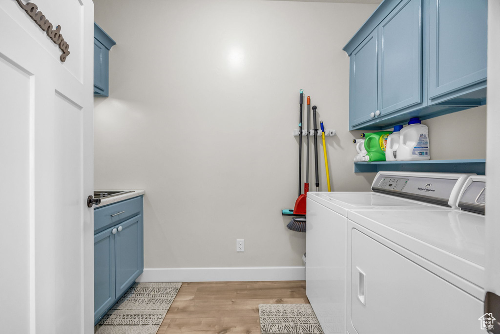 Clothes washing area with baseboards, cabinet space, light wood-style flooring, and washing machine and clothes dryer