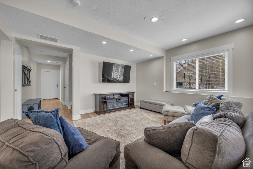 Living room featuring baseboards, visible vents, light wood-style flooring, recessed lighting, and a textured ceiling