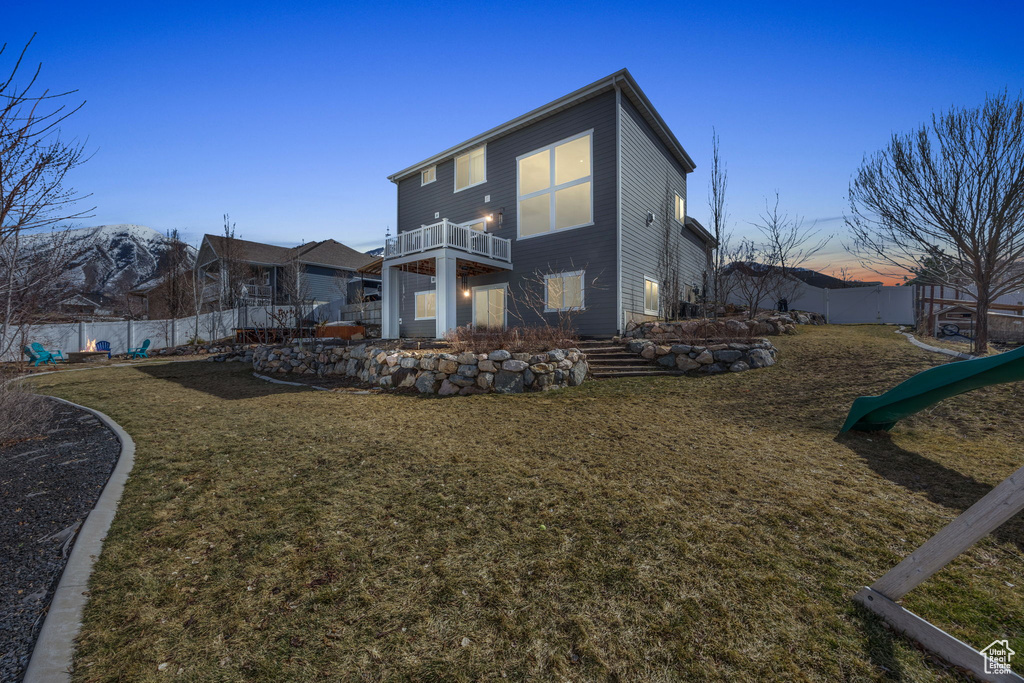 Rear view of house with a balcony, fence, a lawn, and a playground