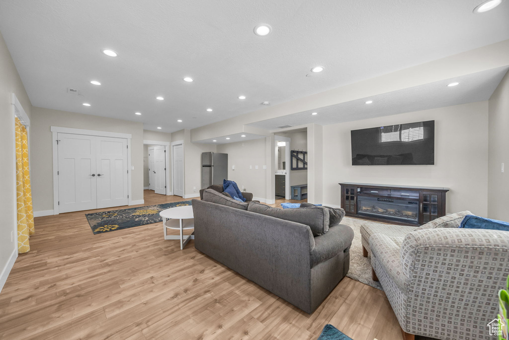 Living area featuring light wood finished floors, a glass covered fireplace, recessed lighting, and baseboards