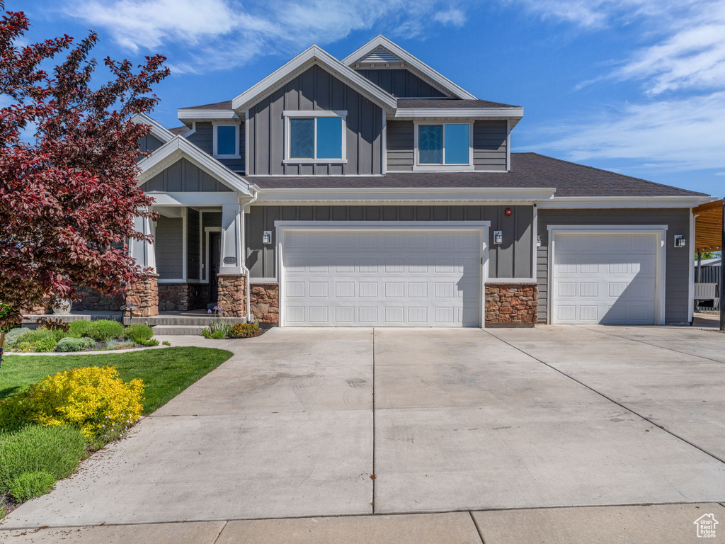 Craftsman house featuring board and batten siding, stone siding, driveway, an attached garage, and covered porch