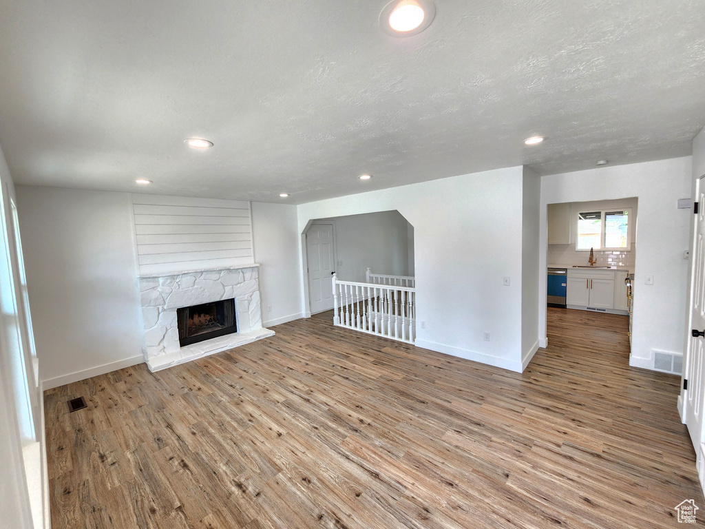 Unfurnished living room featuring wood finished floors, recessed lighting, a fireplace with raised hearth, and baseboards