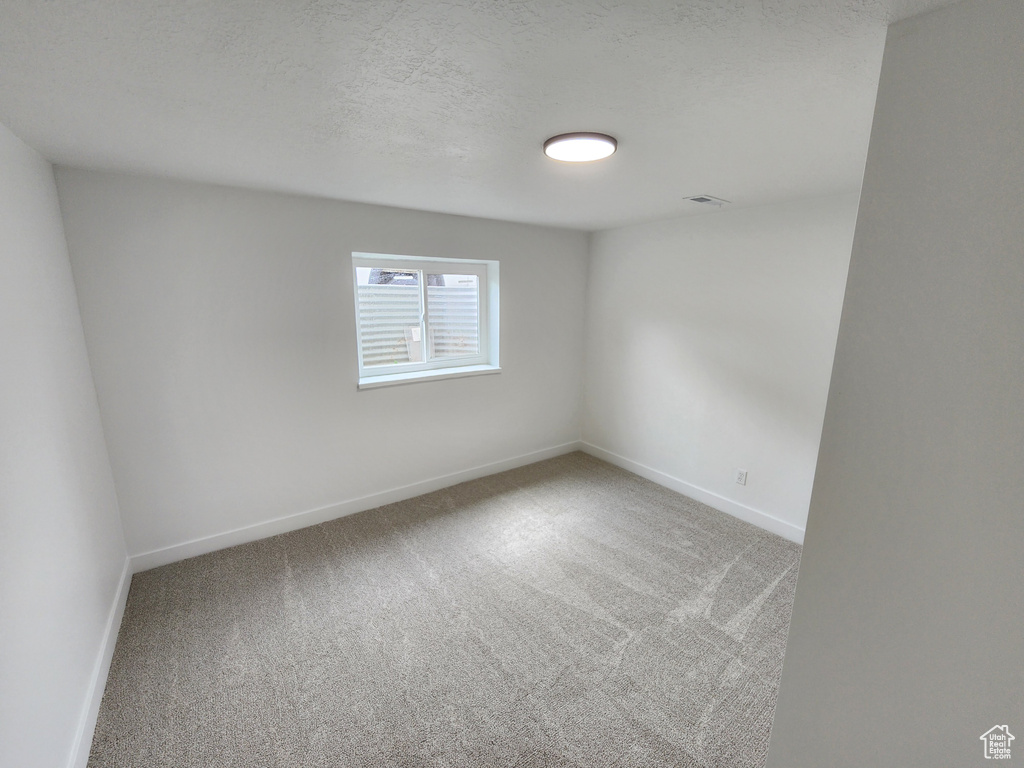 Carpeted spare room with visible vents, a textured ceiling, and baseboards