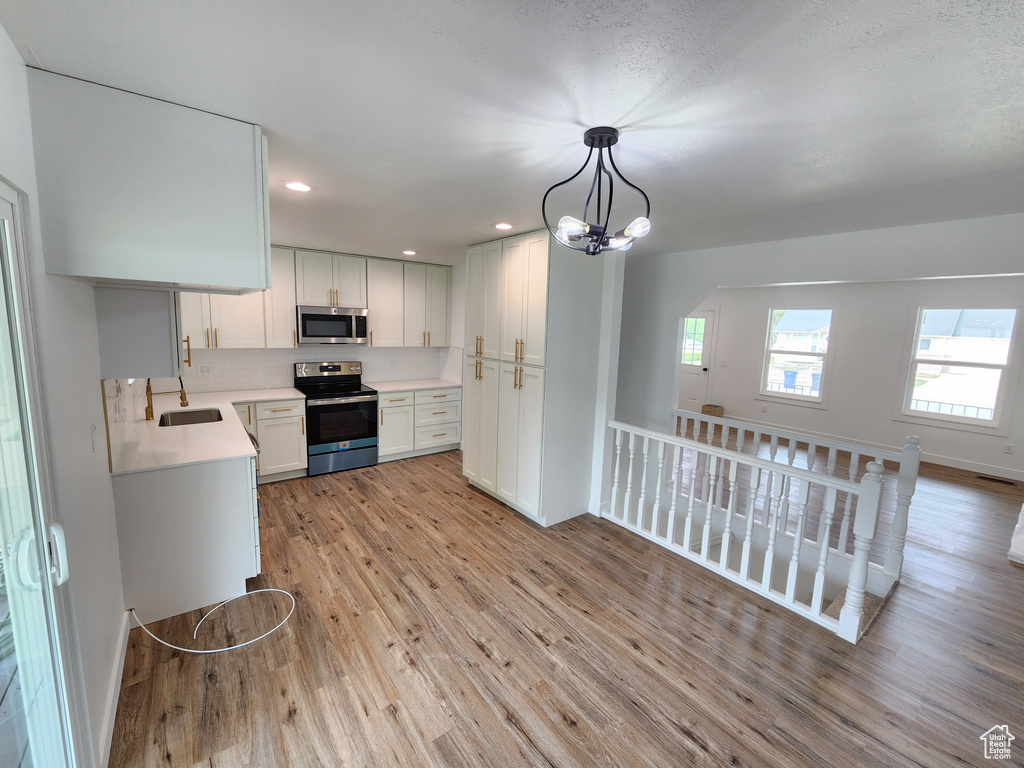 Kitchen with stainless steel microwave, light wood-style flooring, electric stove, a notable chandelier, and a sink