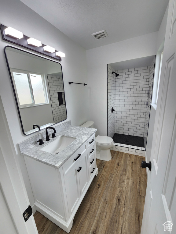 Full bathroom with visible vents, toilet, wood finished floors, tiled shower, and vanity