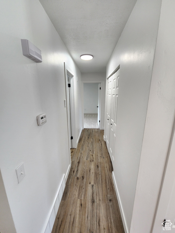 Hall featuring baseboards, a textured ceiling, and wood finished floors