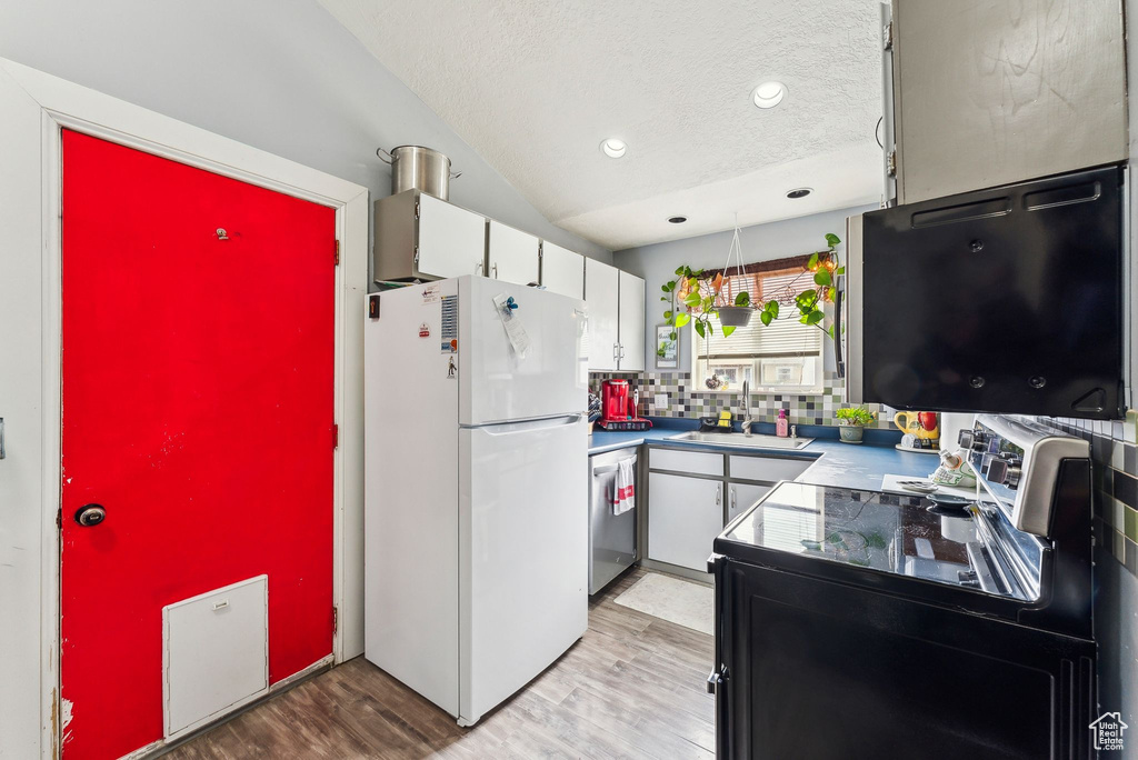 Kitchen featuring a sink, stainless steel dishwasher, white cabinetry, freestanding refrigerator, and light wood finished floors