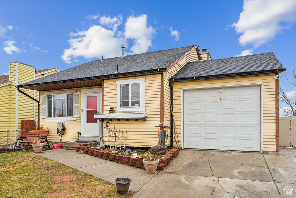 View of front of home with driveway, a chimney, roof with shingles, and fence