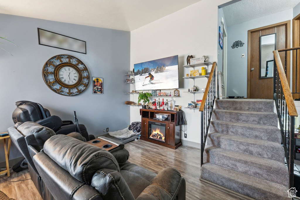 Living room with wood finished floors, a glass covered fireplace, and stairs