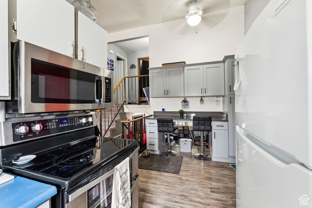 Kitchen with a ceiling fan, wood finished floors, gray cabinetry, stainless steel appliances, and dark countertops