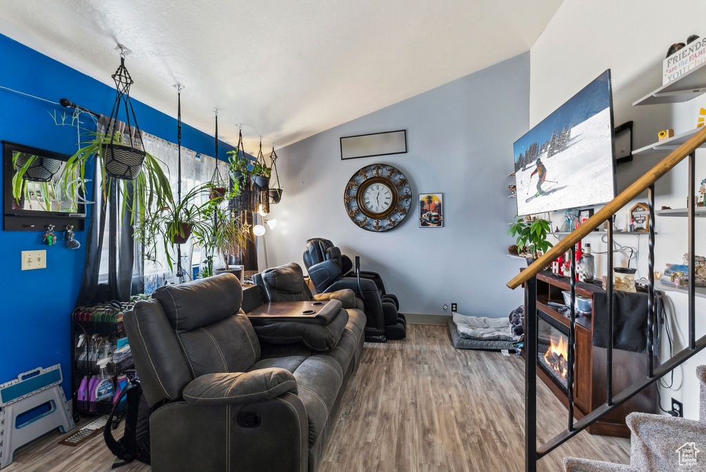 Living room featuring a glass covered fireplace, baseboards, wood finished floors, and vaulted ceiling