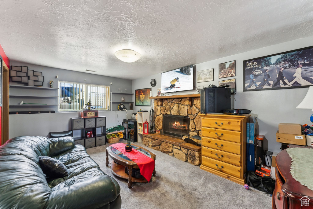 Living room with a stone fireplace, carpet floors, and a textured ceiling