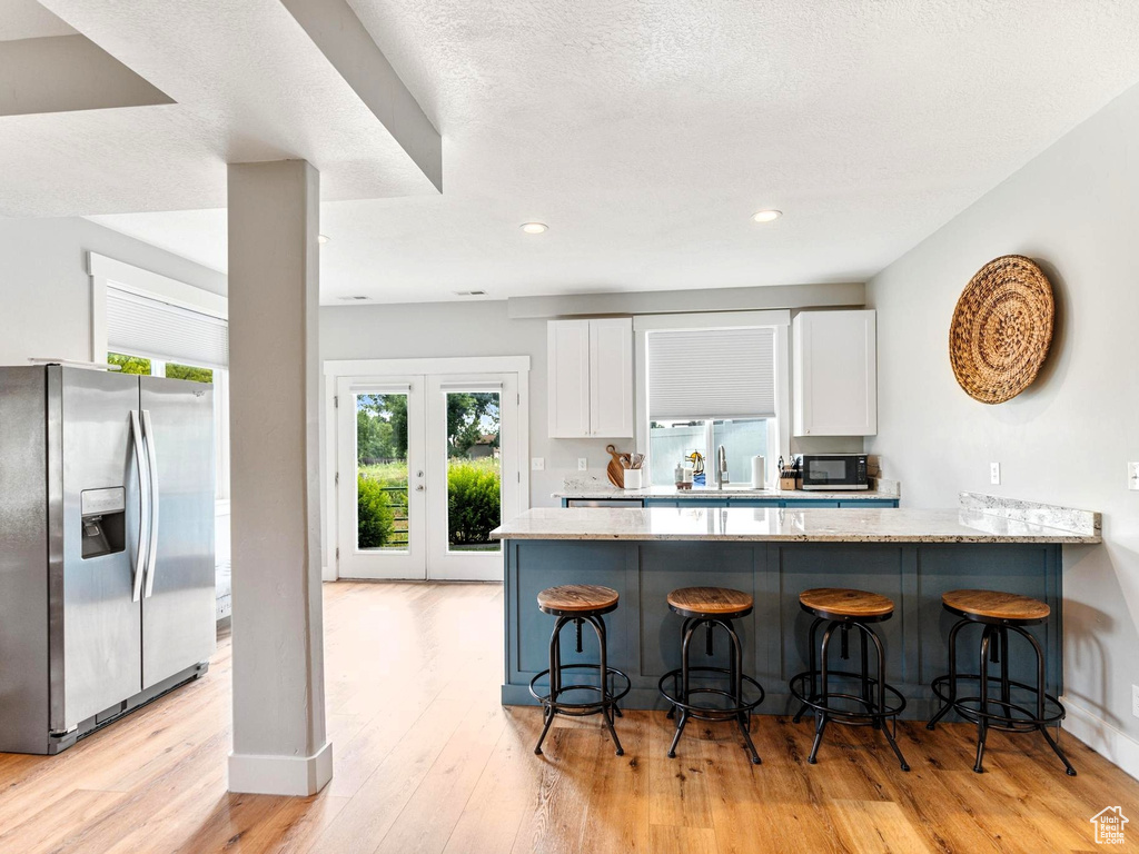 Kitchen featuring light wood-style flooring, a sink, a kitchen breakfast bar, stainless steel fridge, and white cabinets