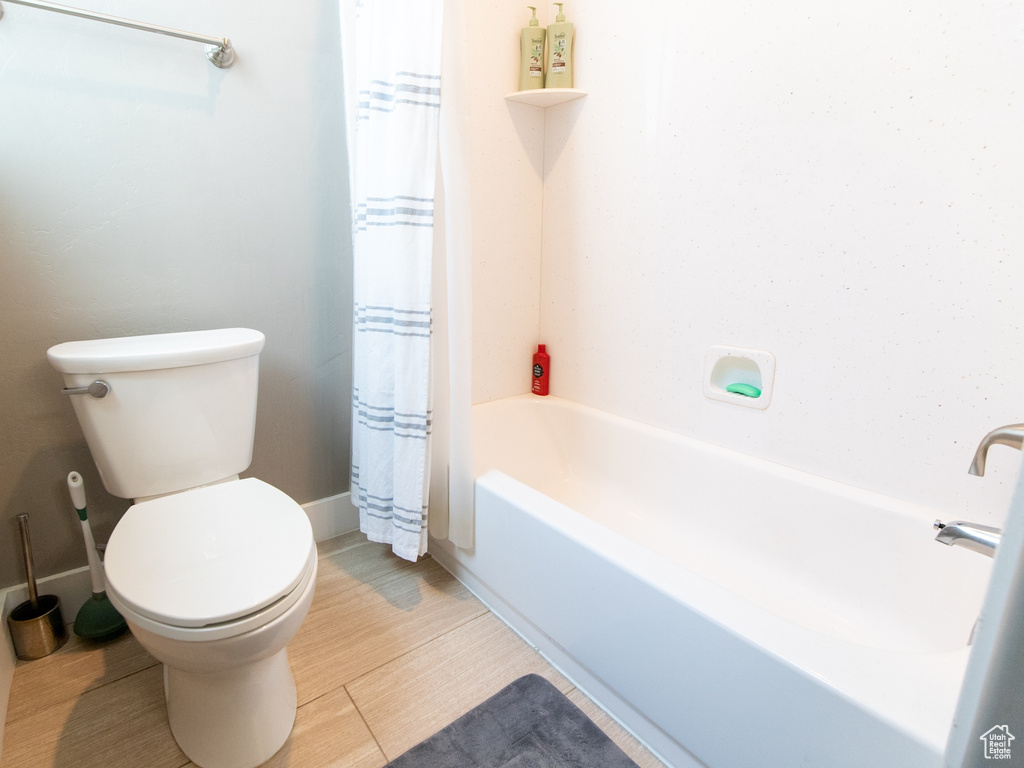 Full bath with toilet, shower / bath combo with shower curtain, baseboards, and wood finished floors
