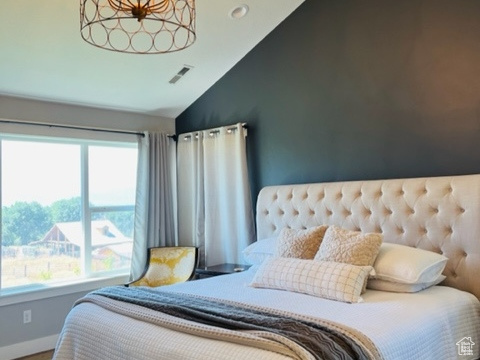Bedroom featuring visible vents, wood finished floors, an inviting chandelier, baseboards, and vaulted ceiling