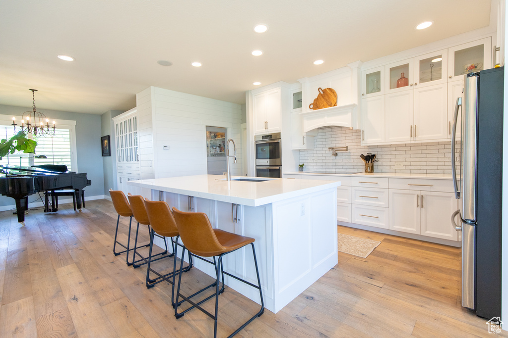 Kitchen with light wood-type flooring, decorative backsplash, appliances with stainless steel finishes, white cabinets, and a kitchen island with sink