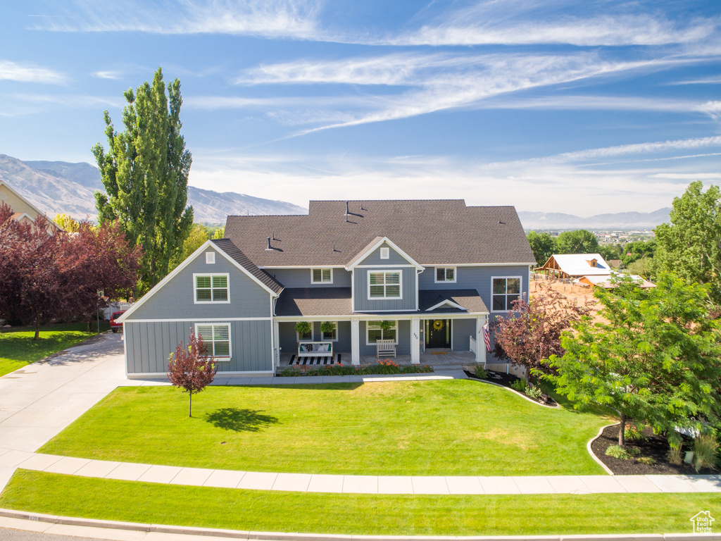 View of front of property featuring a porch, a mountain view, a front yard, and roof with shingles